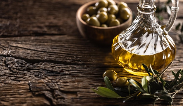 Glass bottle of olive oil and leaves with olives are designed on wooden table