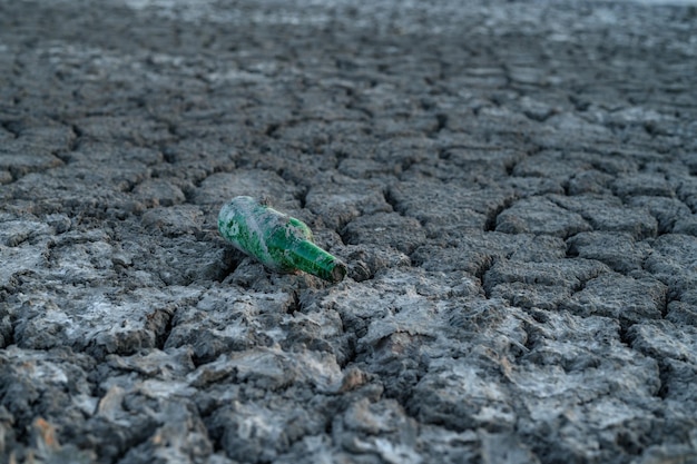 Фото Стеклянная бутылка на потрескавшейся почве высохшего дна озера парниковый эффект изменения климата