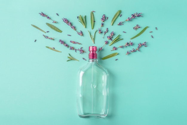 Glass bottle of perfume and leaves and flowers on a green blue background