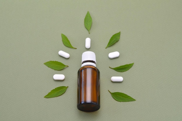 Glass bottle pills and leaves on green background close up