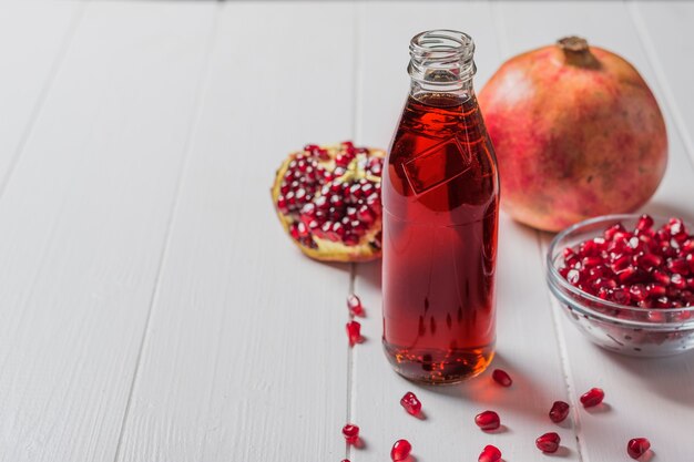 Glass bottle of pomegranate juice with ripe pomegranate fruits on a white table. Drink useful for health.