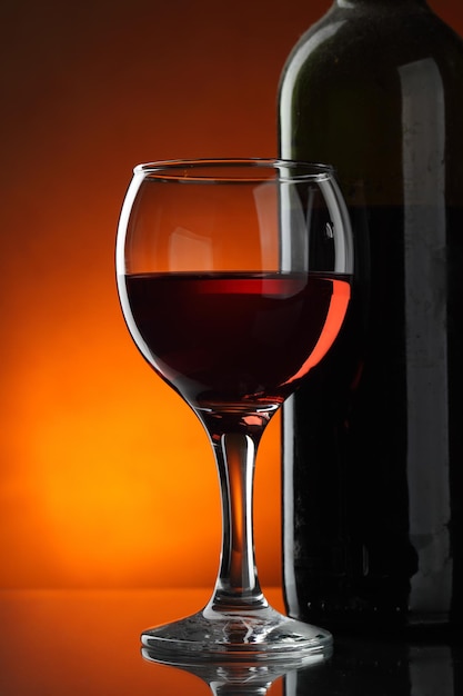 Glass and bottle of red wine over dark red background