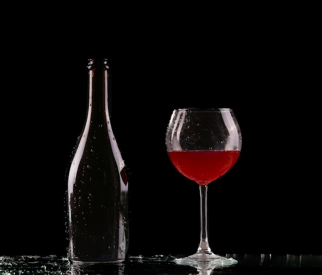 Il vetro e la bottiglia di vino rosso spruzzano sul nero