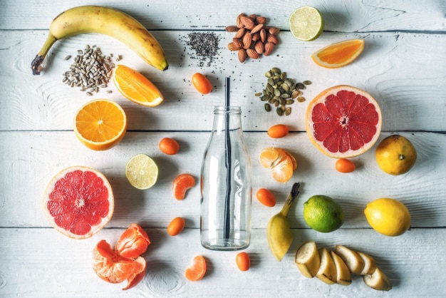 Photo glass bottle surrounded by different fruits and nuts on the white wooden table top view