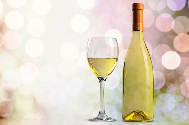 Glass and bottle of white wine on bokeh background