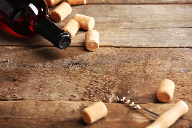 Glass bottle of wine with corks and corkscrew on wooden table background