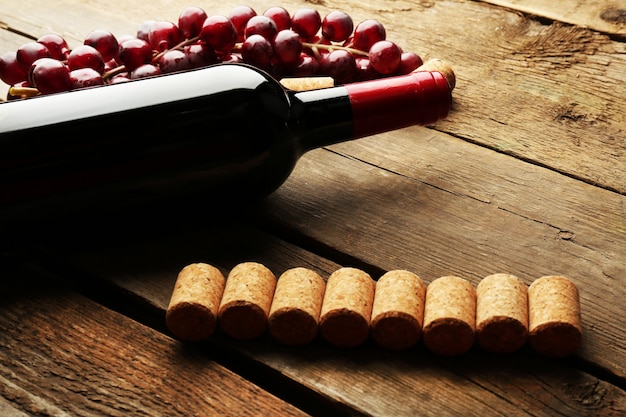 Стеклянная бутылка вина с пробками и виноградом на фоне деревянного стола