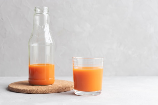 Glass bottle with carrot juice and a glass of juice stand on gray