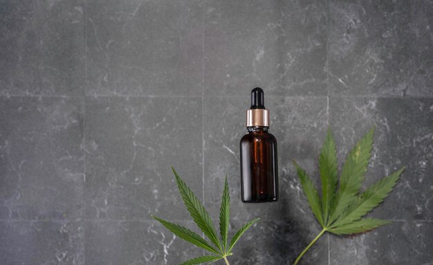 Photo glass bottle with cbd oil thc tincture and hemp leaves on a marble background flat lay minimalism