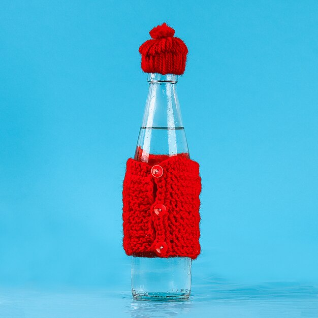 glass bottle with cold water is dressed in a hat and a warm jacket. concept heat and frost.