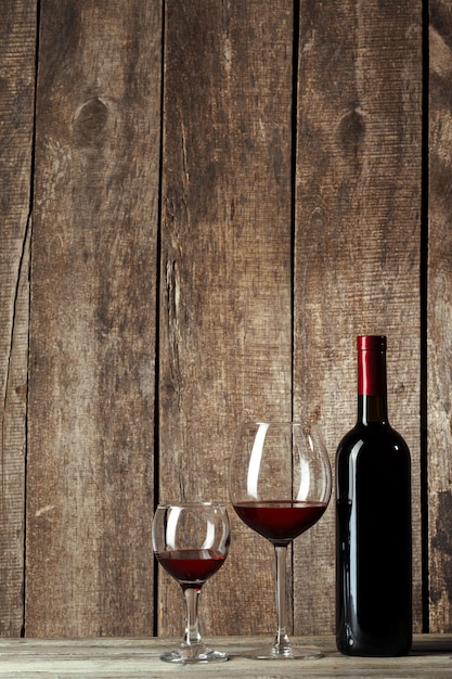 Glass and bottle with delicious red wine on table against wood