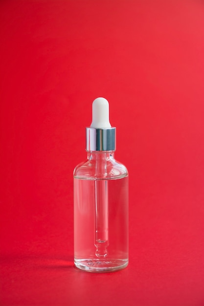 Glass bottle with a dropper on a red background, hard light. liquid face serum with collagen. skin care. copy space.