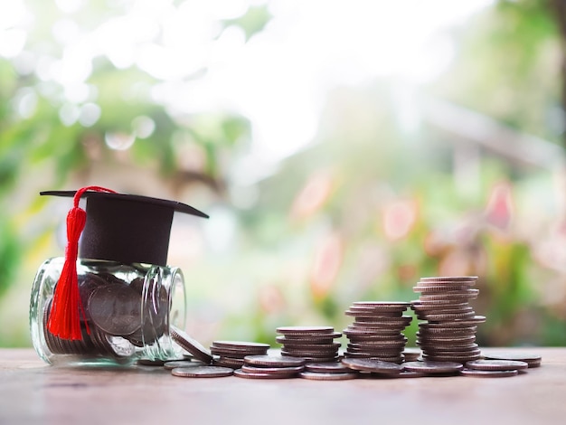 Фото Стеклянная бутылка с выпускной шляпой и стопкой монет концепция экономии денег на образование, студенческий кредит, стипендия, плата за обучение в будущем