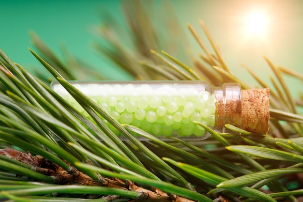 Glass bottle with green granules and a pine branch. homeopathic remedies