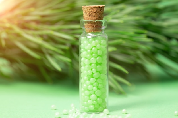 緑の顆粒と松の枝が付いたガラス瓶。ホメオパシー療法