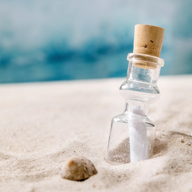 Glass bottle with message paper inside on summer sand sea beach with shell and waves at background Help SOS fate message concept Square image