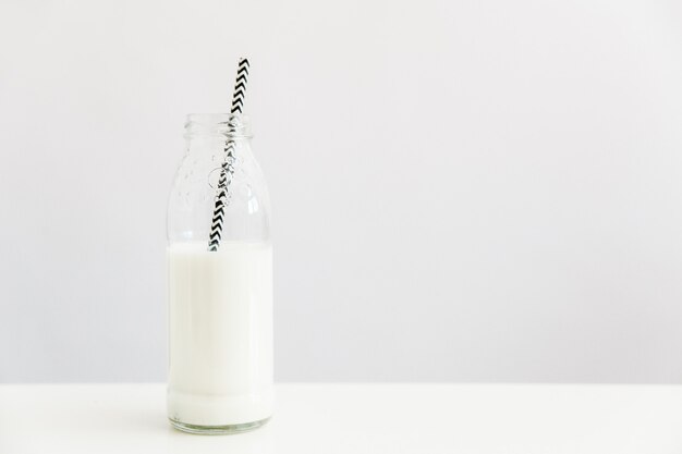 glass bottle with milk and straw on white wall