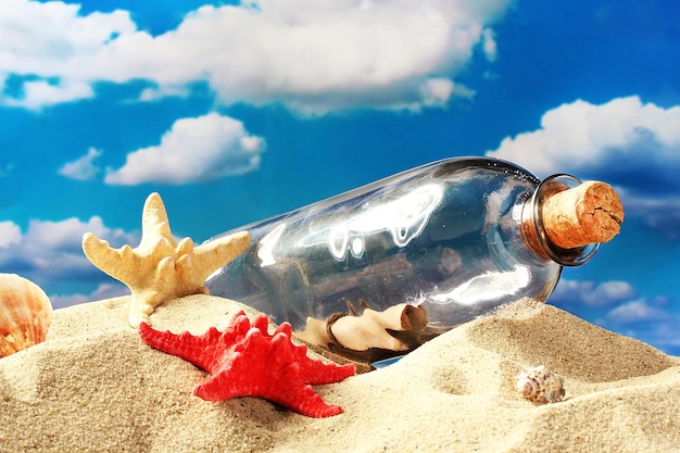 Glass bottle with note inside on sand on blue sky background