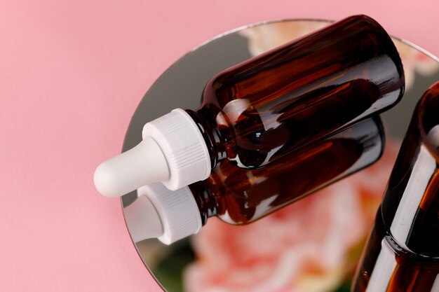 Glass bottle with oil on round mirror on pink close up