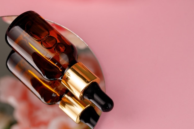 Glass bottle with oil on round mirror on pink close up