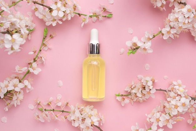 Glass bottle with oil serum on a pink background with blooming cherry Flat lay minimalism Cosmetical tools