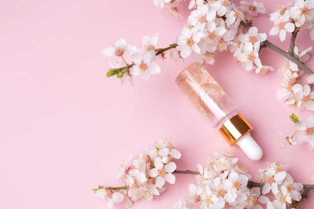 Glass bottle with oil serum on a pink background with blooming cherry