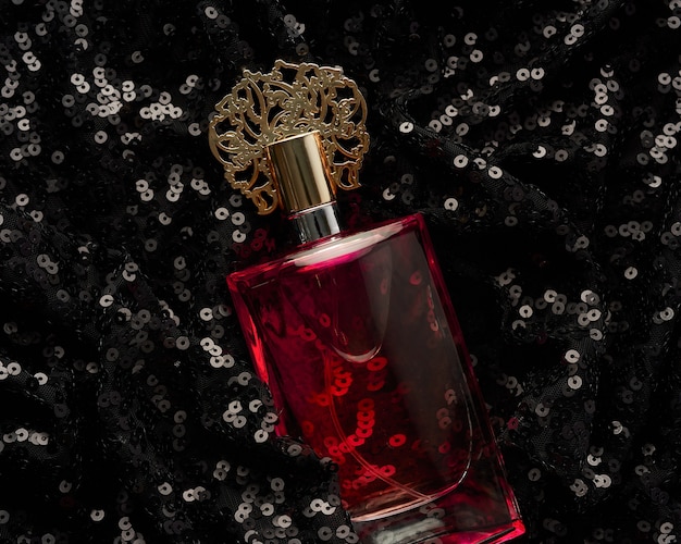 光沢のあるスパンコールと黒の背景にピンクの香水液体とガラス瓶