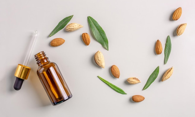 Glass bottle with a pipette and nuts and leaves of almond on a gray background