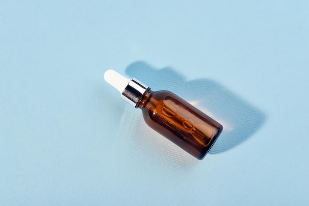 A glass bottle with a pipette with oil serum brown on a blue background Flat Lay