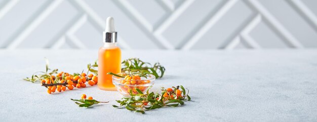 Glass bottle with sea buckthorn oil berries and branches of sea buckthorn on light background