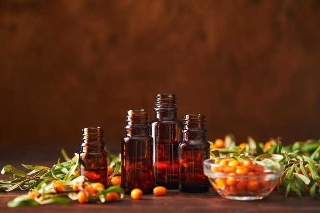 Glass bottle with sea buckthorn oil berries and sea buckthorn branches on wooden background