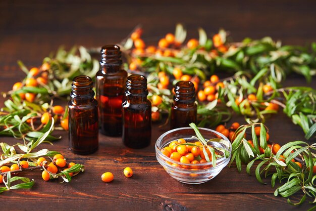 Glass bottle with sea buckthorn oil berries and sea buckthorn branches on wooden background.