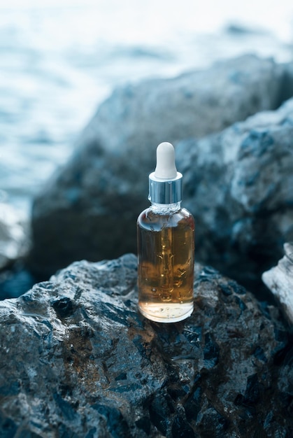 Photo glass bottle with vitamin serum on the rocks on a sea shore