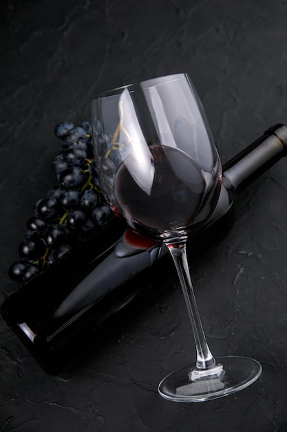 Фото Стеклянная бутылка с вином и темным виноградом на темном фоне