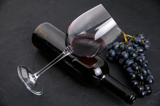 Photo glass bottle with wine and dark grapes on a dark background