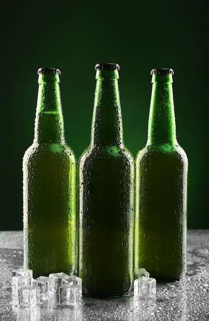 Glass bottles of beer with ice cubes on dark background