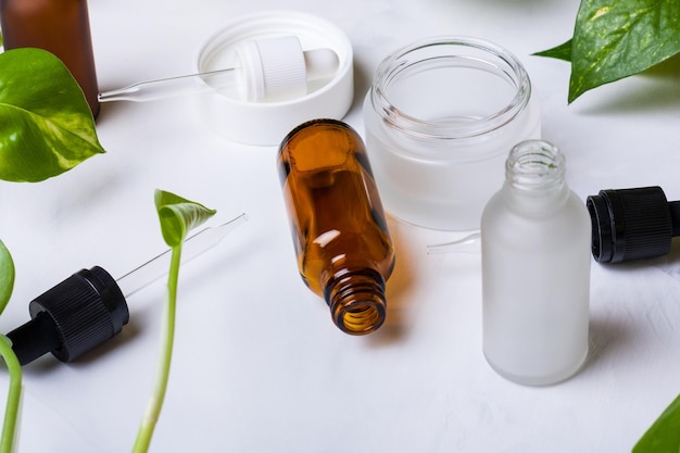 Glass bottles and jar for natural cosmetics on a white marble background