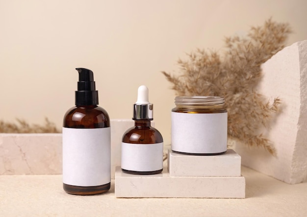 Glass bottles on travertine stone against dry pampas grass on beige close up cosmetic mockup