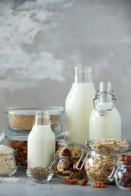 Glass bottles of vegan plant milk and almonds, nuts, coconut, hemp seed milk on grey concrete background. 