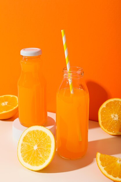 Glass bottles with juice and oranges on orange background