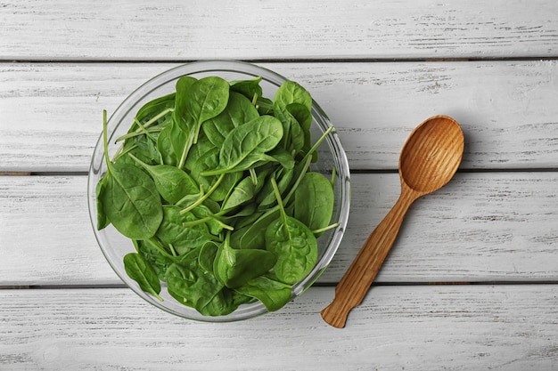 Glass bowl full of fresh spinach and spoon on white wooden table