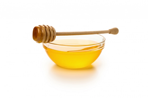 Glass bowl of honey with dipper isolated