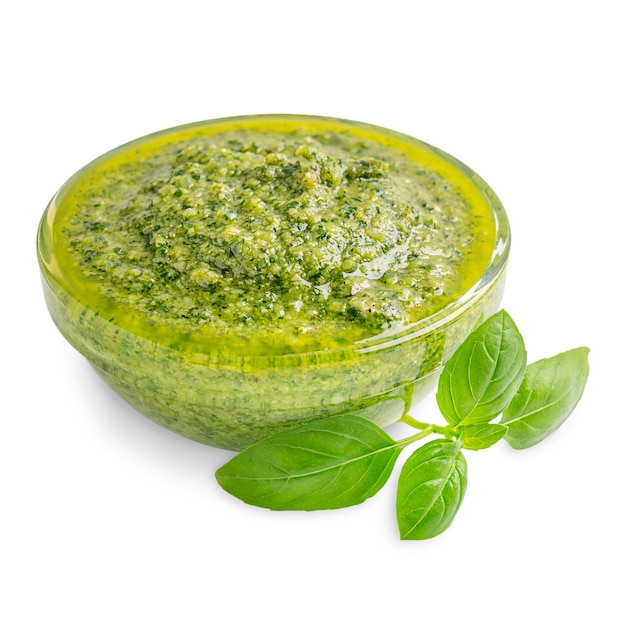 Ciotola di vetro di pesto a base di parmigiano di pinoli foglia di basilico e olio d'oliva isolato su bianco