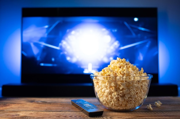 A glass bowl of popcorn and remote control in the background the TV works Evening cozy watching a movie or TV series at home