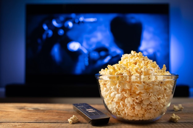 Una ciotola di vetro di popcorn e telecomando in sottofondo la tv funziona