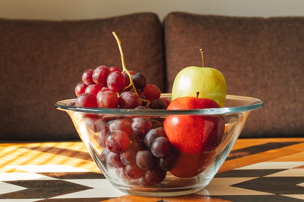 Glass bowl of variety of fruits on wooden table in warm light.
