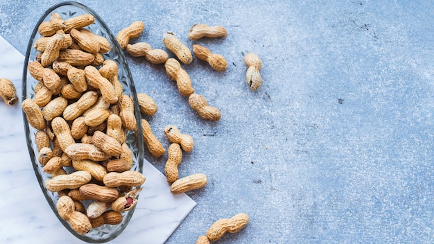 Glass bowl of whole peanuts with shells on granite backdrop