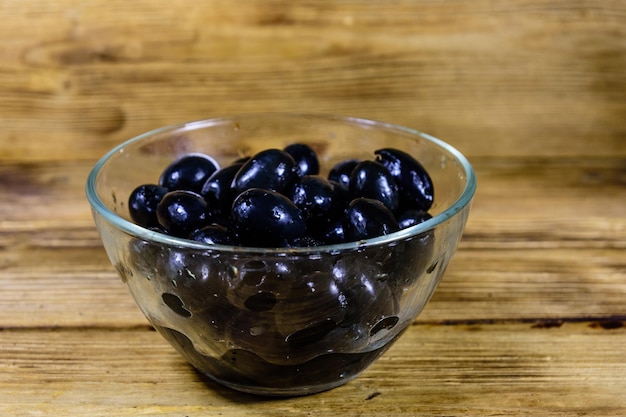 Glass bowl with black olives on wooden table