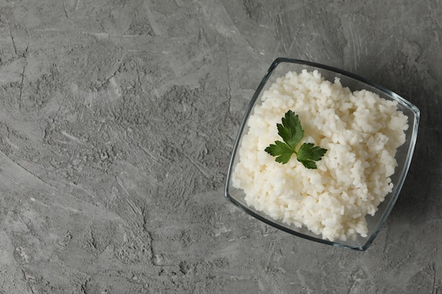 Glass bowl with boiled rice on grey surface