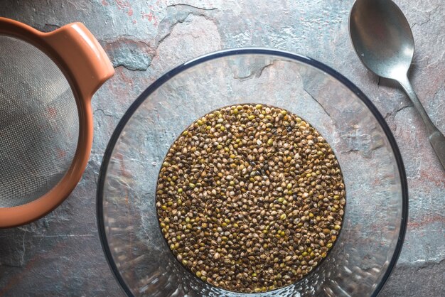 Photo glass bowl with cannabis seeds a sieve and a spoon on a stone table